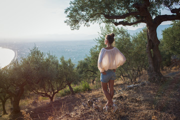 Yong women in olive field meditating  toward the sea on sunset