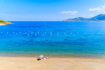 Fototapeta na wymiar Family sunbathing on beautiful beach with azure sea water, Corsica island, France