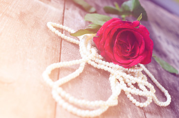 Red rose and pearl necklace on wooden background.