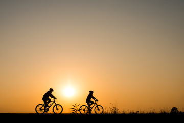 Silhouette of cyclist with friend motion on sunset background
