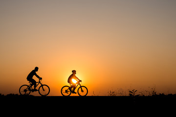 Silhouette of cyclist with friend motion on sunset background