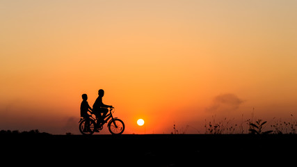 Silhouette of cyclist with friend motion on sunset background