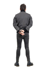 Rear back view of man in tight jeans and gray jacket looking away. Full body length portrait...