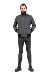 Confident bearded hipster in gray jacket, tight jeans and army boots looking at camera. Full body length portrait isolated over white studio background. 
