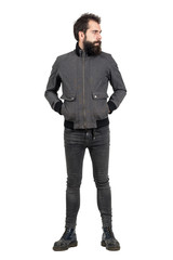 Fototapeta premium Serious bearded punker in gray jacket, tight jeans and old army boots looking away. Full body length portrait isolated over white studio background. 