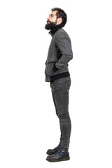 Side view of young bearded punker in old army boots looking up with hands in pockets. Full body length portrait isolated over white studio background. 