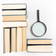 Stack of books with magnifying glass. Search information.