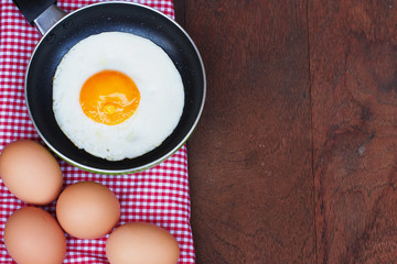 Fried eggs in a frying pan on wooden background