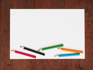 Color pencils and a paper on wooden background