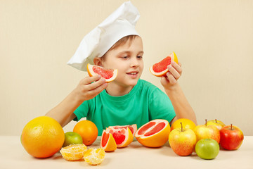 Fototapeta na wymiar Little funny chef with two slices of grapefruit at the table with fruits