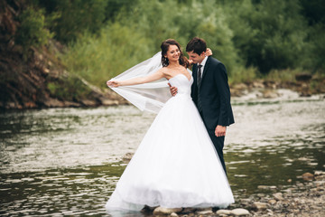 Fototapeta na wymiar Elegant gentle stylish groom and bride near river with stones. Wedding couple in love