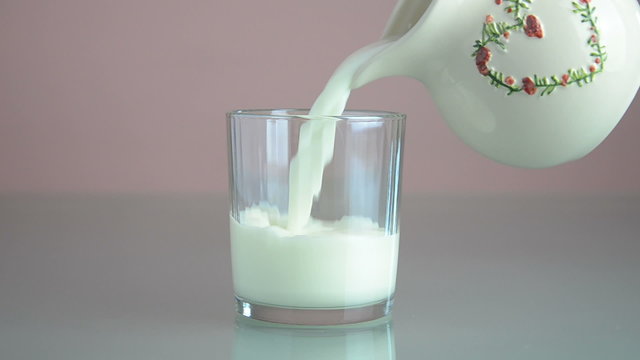 Pouring milk from a white jar with heart shaped ornament, in a glass.