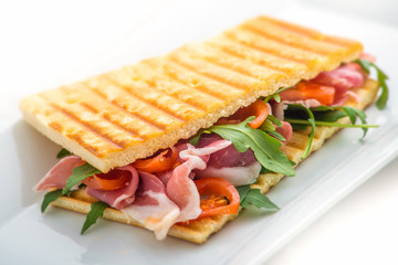 toast sandwich with ham, tomatoes and arugula salad on white plate