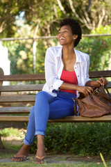 Obraz premium Smiling african woman sitting on a park bench with a bag
