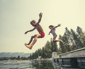 Kids jumping off the dock into a beautiful mountain lake. Having fun on a summer vacation at the lake with friends - Powered by Adobe