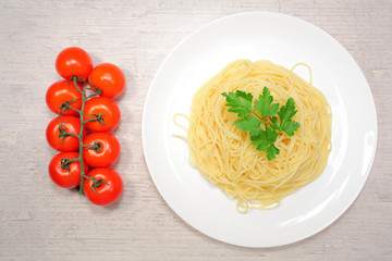 Italian food: pasta on a large white plate next to the red cherry tomatoes and green olives