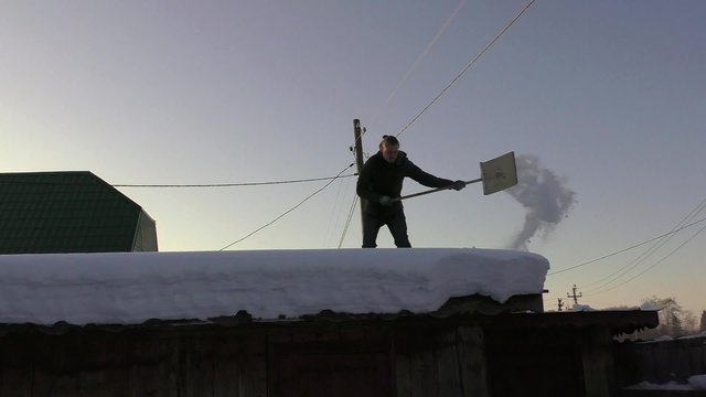 young guy knocks the snow of the roof