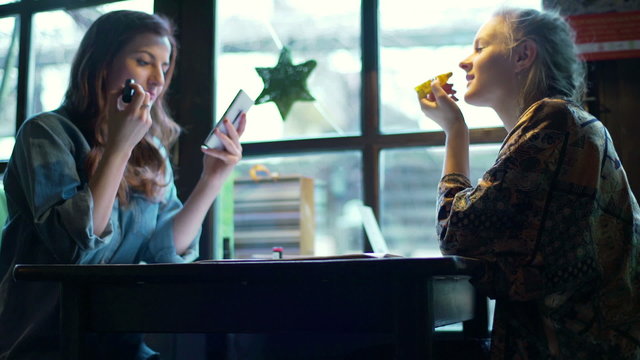 Girl using lip products in the cafe and waiter bringing their order
