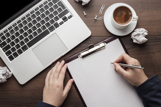 view from above businesswoman writing. brown wooden office table with cup of coffee, notepad and laptop computer - Powered by Adobe