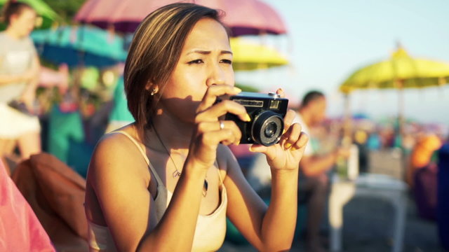 Young woman taking photo with retro camera sitting on the cafe by the beach 
