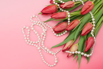 

Red tulips and necklace on pink background