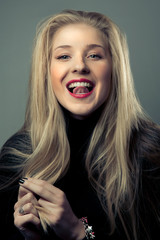 Portrait of emotional blond girl with hand near her face in black wear in studio with dark background