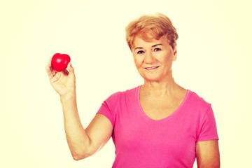 Old smiling woman holding red toy heart 