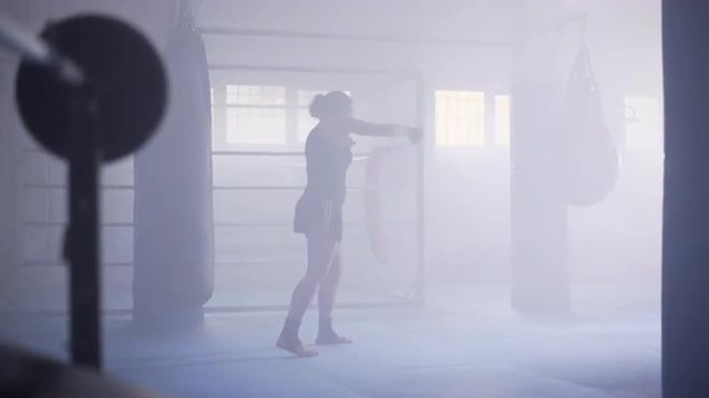 Female boxer shadowboxing in a boxing club with a ring at background. Dolly move. UHD, 4K.