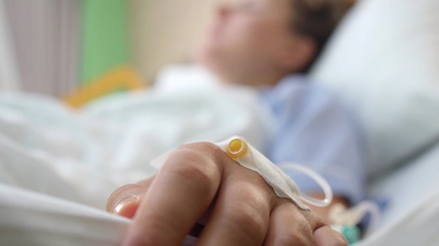 Patient Hand In Hospital Bed Having Drop Bottle Close Up