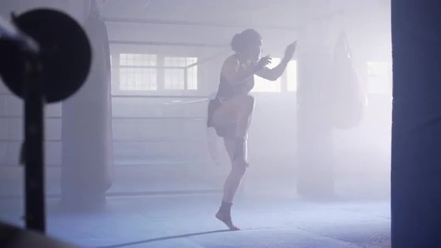 Female muay thai boxer shadowboxing in a boxing club with a ring at background. Dolly move. UHD, 4K.