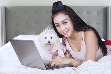 Female model uses notebook with dog on bed