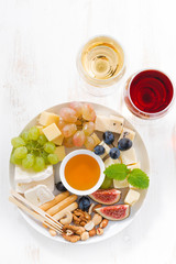 Fototapeta na wymiar cheeses, fruits, wine and snacks on plate, vertical top view