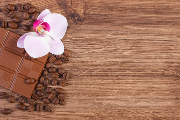 Milk chocolate, coffee grains and blooming orchid, copy space for text
