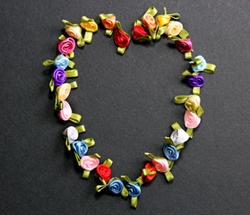 Miniature satin Rose flowers in the form of a heart on a grey background.