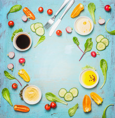 Various salad and dressing ingredients on light blue background, top view, frame.