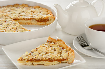 Piece of pie with carmel and almond. and cup of tea.