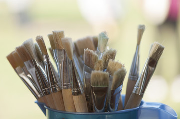 Painting brushes in a plastic recipient near a window