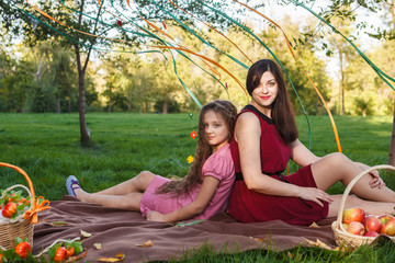 Mom and daughter in the park sitting back to back on a plaid