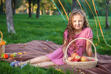 girl sitting on the plaid in the park with a basket of apples