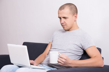 young handsome man sitting on sofa with computer and cup of tea