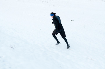 Healthy young man jogging outside on snow, athlete running on winter day