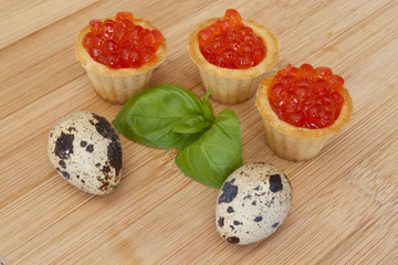 Red caviar tartlets, eggs on the wooden background