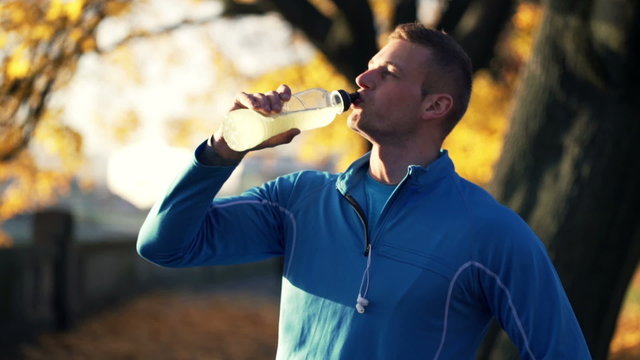 Man drinking isotonic drink after workout, in the autumn park
