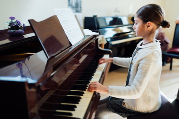 beautiful schoolgirl playing piano at  music school
