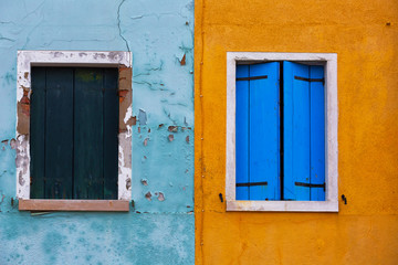 Fototapeta na wymiar Old walls of blue and orange with the windows closed shutters, Burano, Venice