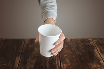 Woman hand holds paper glass above table