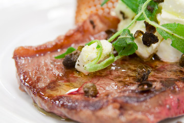 Rare cooked steak with capers and cheese topping