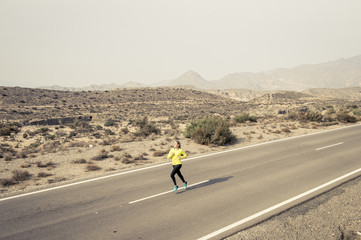 young attractive sport woman running on desert mountain asphalt road
