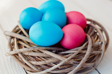 blue and pink Easter eggs in nest on white wooden background