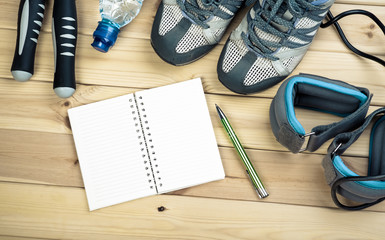 Skipping Rope, Ankle Weights, Sport Shoes, Bottle Of Water And Notepad To Workout Plan On Wooden Table. Sport Fitness Background